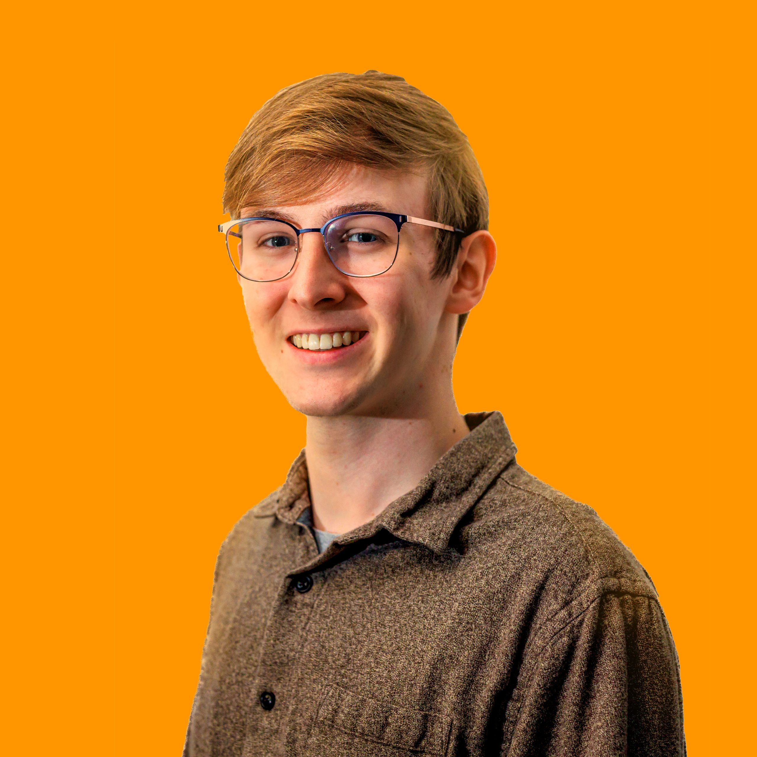 A photograph of a caucasian man staring into the camera with wide eyes and an open mouth. He wears glasses and has dirty blonde hair brushed to the side.